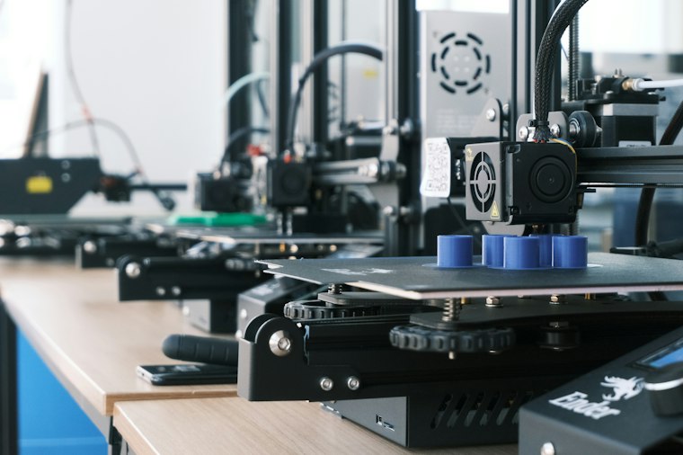 Row of 3D printers printing identical blue parts